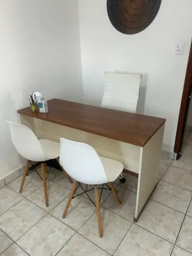 Mesa para escritório, cadeira de rodinhas branca e duas cadeiras com pé de madeira .