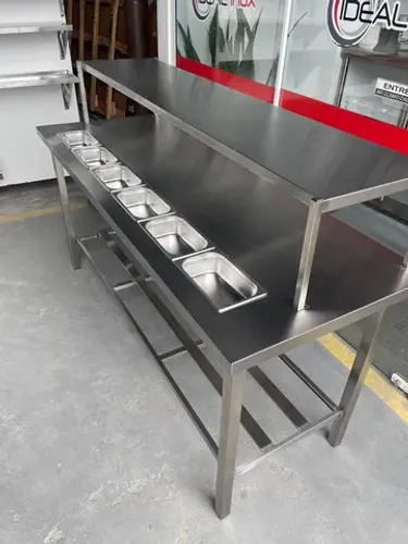 Mesa industrial com condimentadora de bancada e prateleira de apoio.
