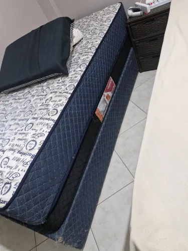 Cama de solteiro com colchão e cômoda.