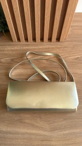 Bolsa carteira (clutch) de festa dourada com acabamento liso e alça fina transversal.