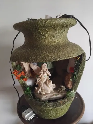 Fonte em formato de jarra aberta, com cristais diversos, escultura de anjo e iluminação.