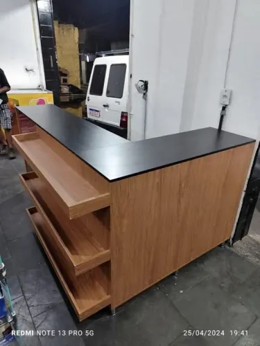 Balcão personalizado em L amadeirado com tampo preto, pés de inox