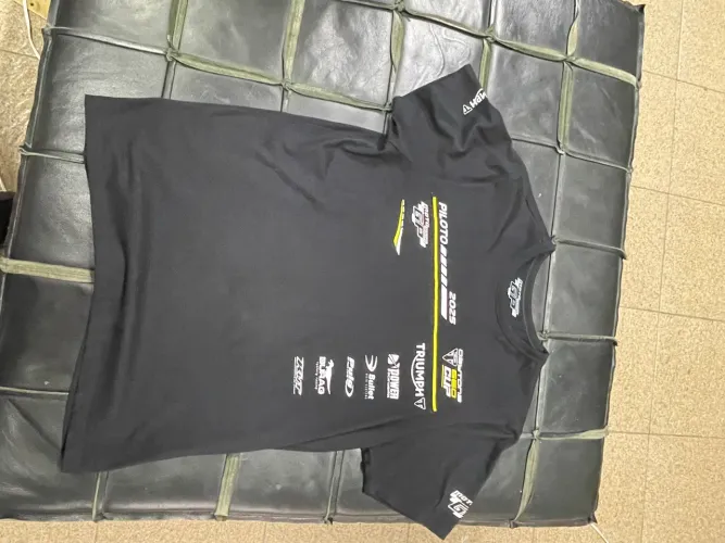 uma camiseta preta com estampas de patrocinadores do Triumph GP 2025